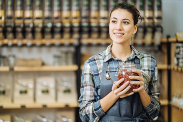 Concept of zero waste shop. Woman holding large glass jar with groceries on interior background of...