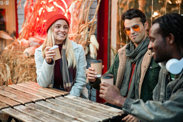Happy friends sitting with coffee cups outside