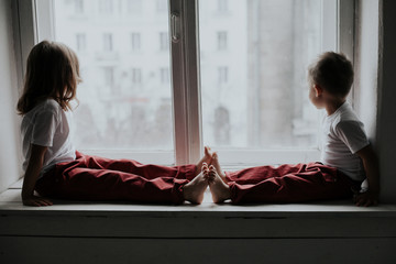 little boy and girl sit on the windowsill looking out the window