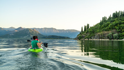 active couple doing kayak at sunset in lake skadar, (Scutari Shkodër Shkodra) on the border of Albania and Montenegro. Perfect reflection like a mirror in the lake. - obrazy, fototapety, plakaty