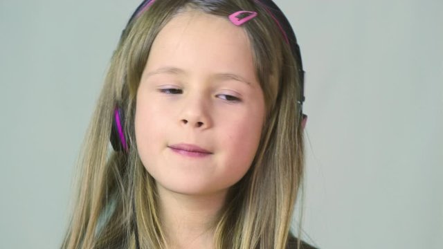 Pretty smiling cild girl listening to music in big pink earphones.