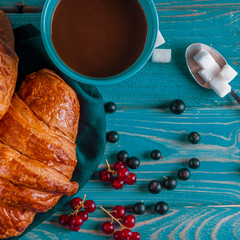 Fresh ruddy croissants with berries lie on a wooden table next to fresh black currant berries, red currants