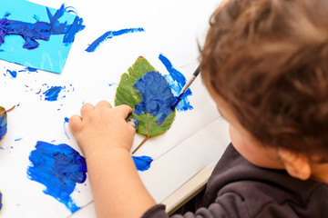 Little child painting leaves blue color, crafts and art therapy. Classic Leaf painting art. Child of stock contributor painting green leaves trendy blue color 2020.