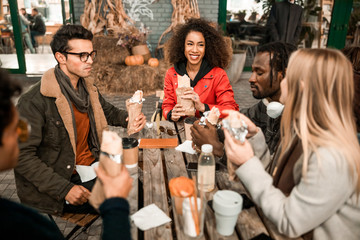 Happy young friends sitting in street cafe with snacks