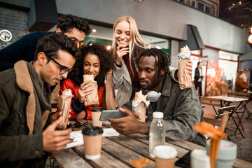 Smiling young friends eating snacks in street cafe