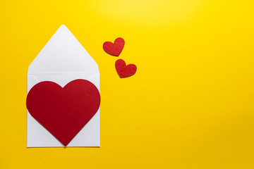 Valentine’s Day greeting card with white envelope and decorative red hearts on bright yellow background with copy space for your text.