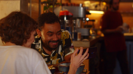 Slow motion, friends sit at a table in a cafe, they look at phone and laugh