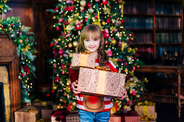 Obraz na płótnie Canvas Beautiful blonde girl stands at the Christmas tree with gifts. Holidays, sale concept.