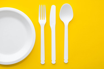 Plastic white fork, knife, spoon and plate on yellow background. Cooking utensil. Top view. Minimalist Style. Copy, empty space for text
