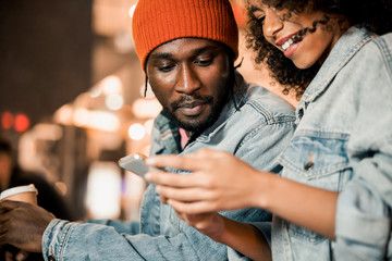 Happy Afro American couple looking at gadget screen outdoors