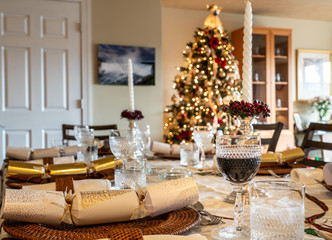 Traditional british christmas lunch table setting with crackers and glasses with xmas tree in the background