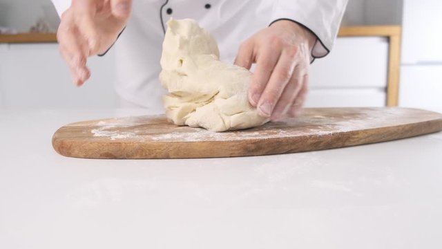 Male hands kneading dough in flour on a table and wooden board. Close up.