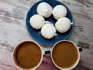 close-up of large cups with coffee / cocoa and white marshmallows on a blue plate on a background of abstract wooden surface