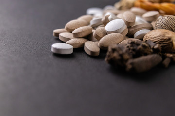 Herbal medicine concept. macro shot of white and brown tablets with dried herbs on a black background with copy space