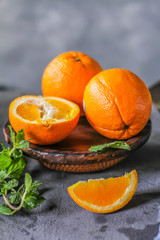 Photo of fresh orange on retro background. A slice of orange with green leaves. Half of orange on wooden plate bowl. Free space for text. Dark background. Image