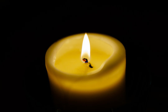 Photography of burning candle with a black background. The concepts of life, memory, farewell. Close up image of top of big yellow candle .