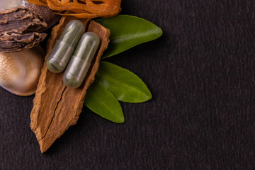 Macro shot of two green herbal capsules on a cinnamon stick and green leaves on black background with copy space. Herbal medicines concept