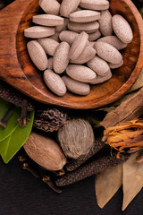 Top view cose up of herbal medicines in a serving spoon with green leaves, nutmeg, and other herbs on black background. Unani medicine concept