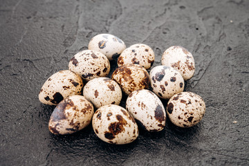 Obraz premium Quail eggs on a black background. Several quail eggs lie on a black stone background