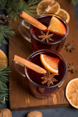 Red spicy Christmas mulled wine in two glasses with orange slices on the basis of red wine with spicy cinnamon sticks, star anise, on a black background. The view from the top.