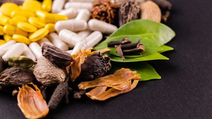 Traditional medicine concept. Whole spices and green herbs with herbal pills on a black background