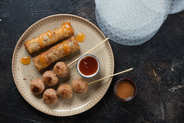 Nem nuong or fried vietnamese meatball skewers with nems on a beige plate. Flatlay over dark brown stone background, horizontal shot