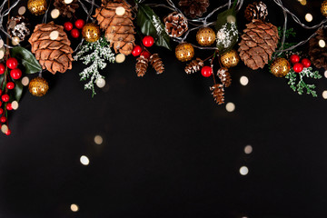 Golden garland, forest pinecones, red berries and green leaves in snow on the black background with multicoloured lights.