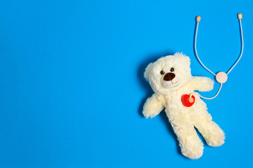 White teddy bear with toy stethoscope on a light blue background. Top view. Copy space for text