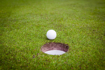 Golf ball on green meadow. golf ball on lip of cup