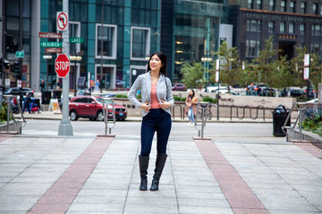 Obraz premium Chicago,IL/USA- November 10th 2019:a happy Asian business woman with long black hair wearing a comfortable trendy fall sweater is walking confidently carrying a fashionable handbag in downtown area