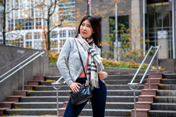 Chicago,IL/USA- November 10th 2019:a happy Asian business woman with long black hair wearing a comfortable trendy fall sweater is walking confidently carrying a fashionable handbag in downtown area