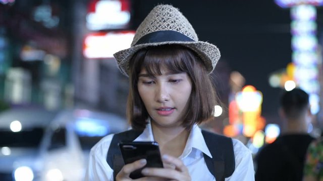 Travel concept. Beautiful girls are playing mobile phones to have fun in the city at night. 4k Resolution.
