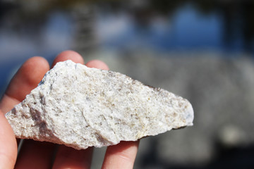 Close up hand holding rock on a background of blue color water with landscape sky and trees reflection