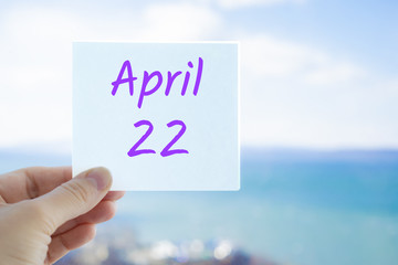 April 22nd. Hand holding sticker with text April 22 on the blurred background of the sea and sky. Copy space for text. Spring month in calendar concept