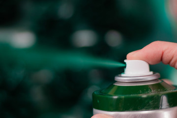 Green spray paint. Green spray from a spray can. Blurred turquoise background. A finger presses on...