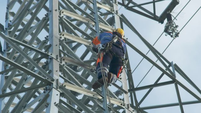 Utility worker climbs up high electrical pole to perform maintenance. 
