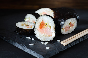 rolls with rice fish and tomato on a stone board, japanese food on a dark wooden background and chopsticks