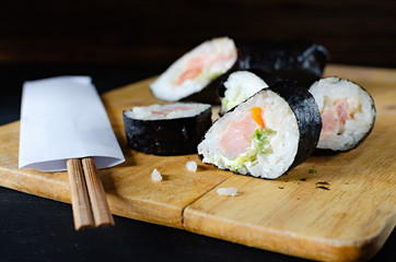 rolls with rice fish and tomato on a wooden board, japanese food on a dark wooden background and chopsticks