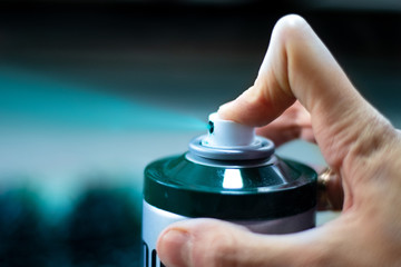 Green spray paint. Green spray from a spray can. Blurred turquoise background. A finger presses on the spray gun, paint is sprayed.