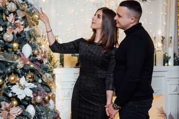 Lovely couple couple decorates Christmas tree at home, while celebrating New Year's Eve. People, family and leisure concept - couple at night at home. New Year holiday concept