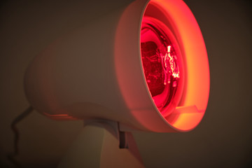 Close up of infrared lamp glowing in the dark with its warming red light to cure for example colds or tensions.