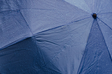 Close up of rain drops on open umbrella, blue color.