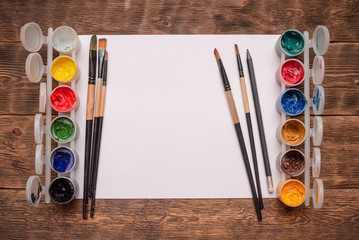 Empty white page with copy space, gouache jars and paint brushes on painter desk background.