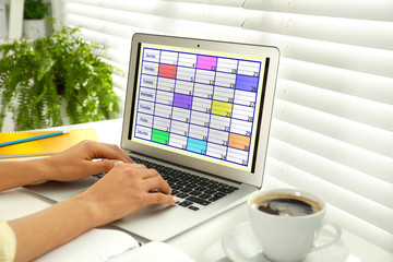 Fototapeta premium Young woman using calendar app on laptop in office, closeup