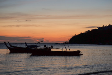 Silhouette group of traditional long tail boats floating in the sea with twilight of sunset and island in background