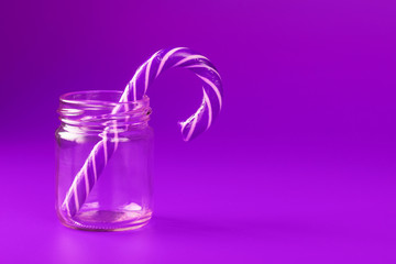 One Lollipop Candy cane in a glass jar on a purple background.