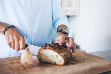 Adult man slicing fresh round bread on wooden cutting board