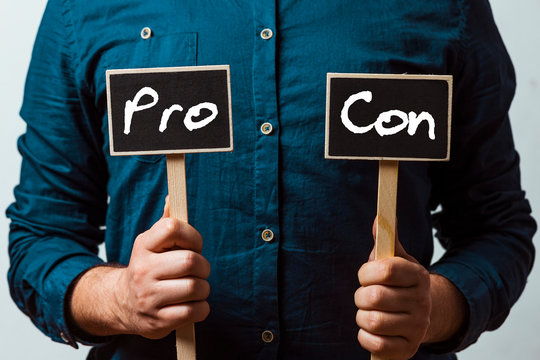 man holding two chalkboards with Pro and con