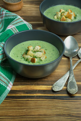 Creamy spinach soup with crackers, herbs and chia seeds. Green soup served in a bowl on a wooden table.