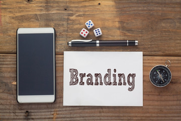 Branding Word written on white on wooden desk with dice,compass,smart phone and pen.Top view conceptual